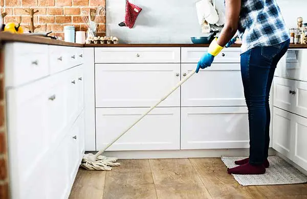 a woman engaged in properly cleaning a house for an open house showing with a mop
