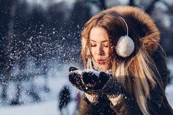 adult blowing light snow off her mittens