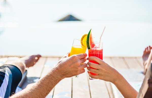 a couple finished with looking through brantford homes for sale is relaxing on a dock overlooking the ocean, giving cheers with some fruity alcoholic beverages