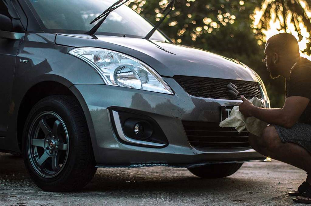 man cleaning his grey suzuki car in the afternoon light 